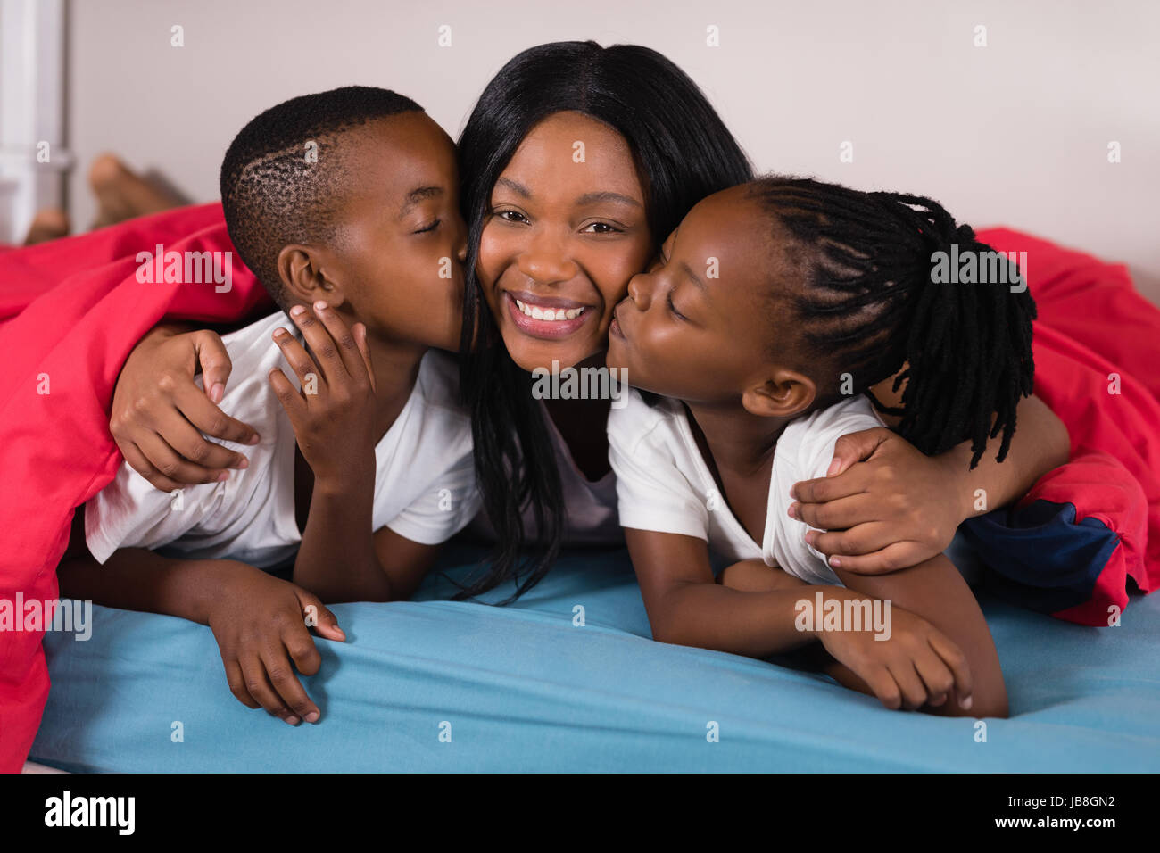 Hermanos besando a su madre mientras está acostada en la cama en casa Foto de stock