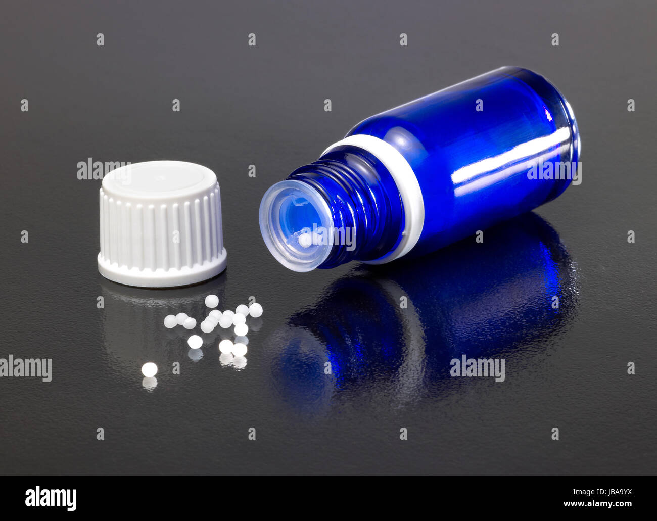 Una pequeña abierta y el tapón en la botella azul oscuro suelo reflectante con glóbulos alrededor Foto de stock