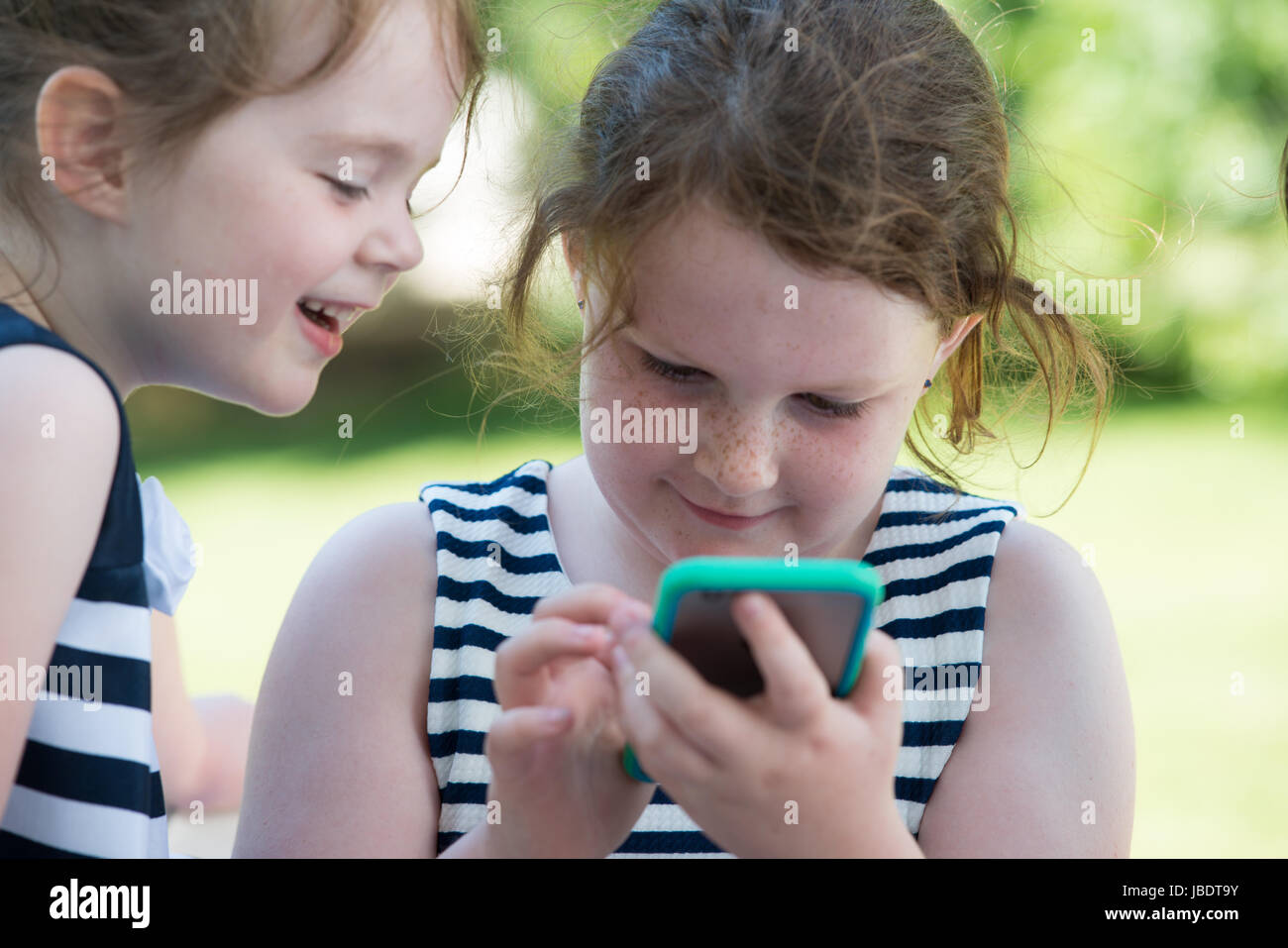 Feliz riendo niños jugando con el smartphone fuera Foto de stock