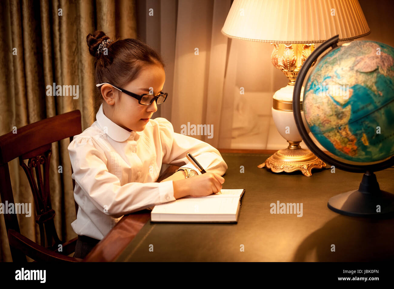 Niña escribiendo en el portátil en el escritorio con lámpara y globe  Fotografía de stock - Alamy