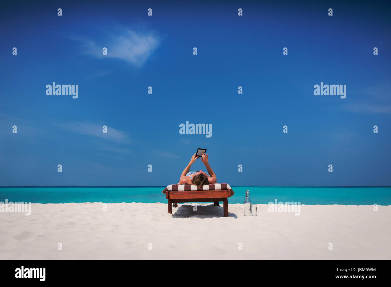 Mujer de relax, tomar el sol, acostado en un sillón y utilizando tablet digital en la soleada playa tropical Foto de stock