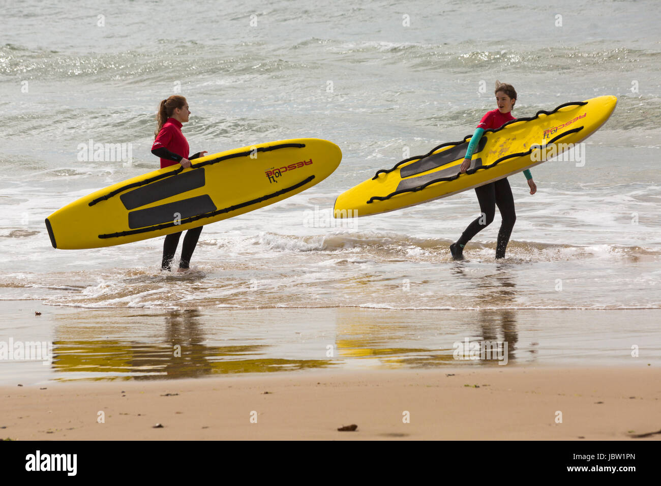 Dos mujeres socorristas Bournemouth llevando vida trineos tablas de surf en el mar en la playa de Bournemouth, Dorset en junio Foto de stock