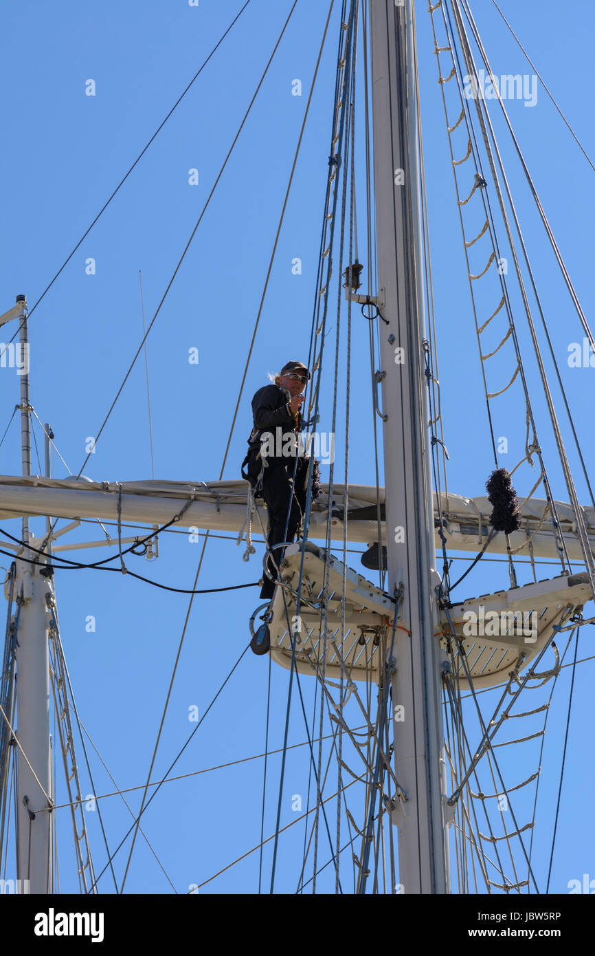 Un marinero femenina trabaja en el aparejo en lo alto de un mástil de yates en Weymouth Harbour, Weymouth, Dorset, Inglaterra, Reino Unido. Foto de stock