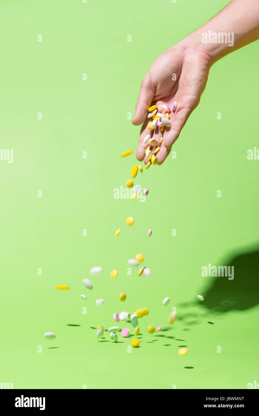 Pastillas de colores cayendo de mano sobre fondo verde. Foto de stock