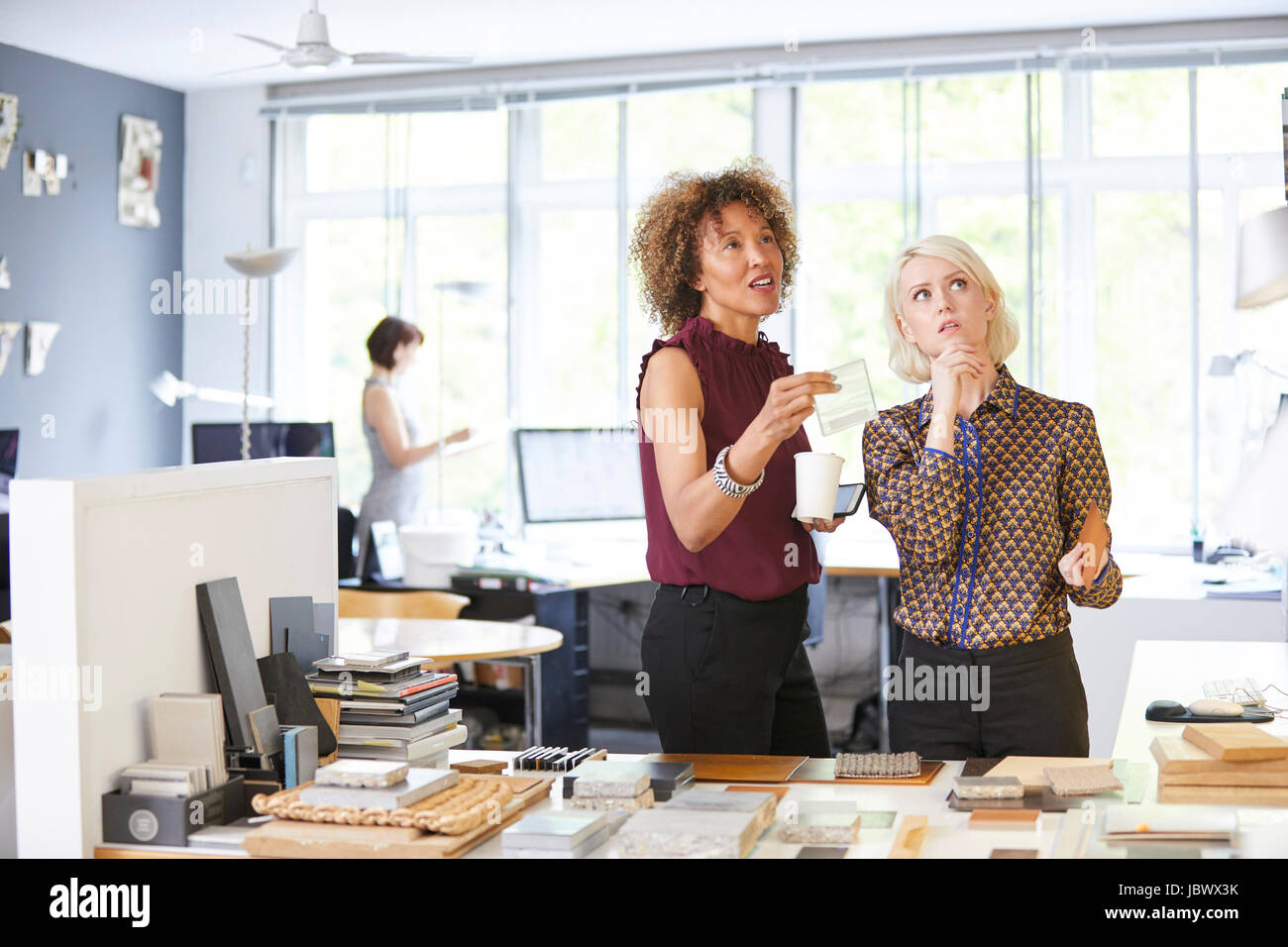 Dos mujeres de diseñadores de interiores considerando muestras de escritorio de oficina Foto de stock