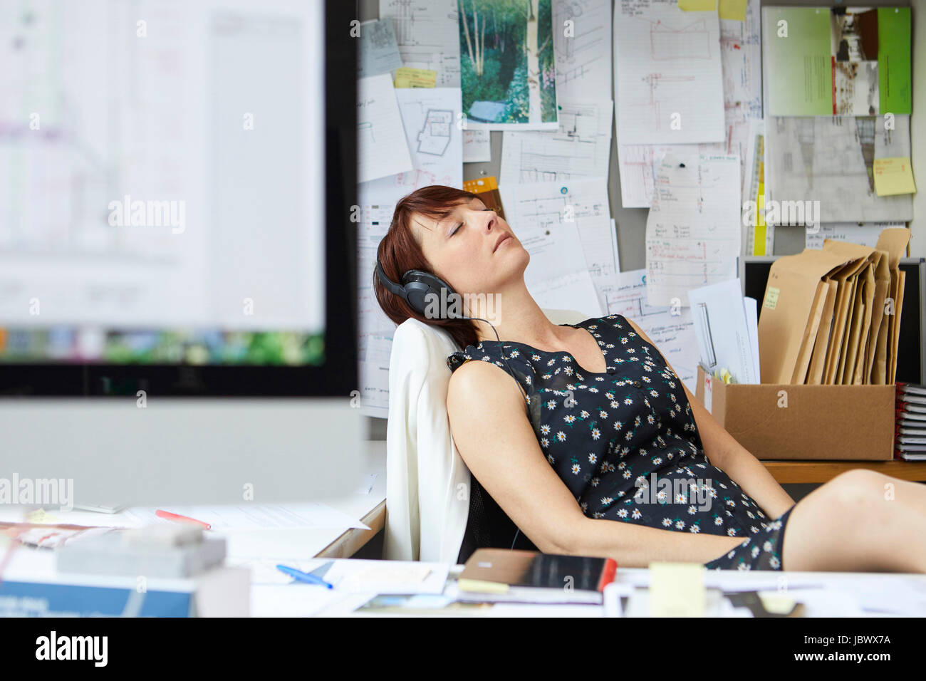 Diseñador femenino en la oficina escuchando música auriculares con los ojos cerrados Foto de stock