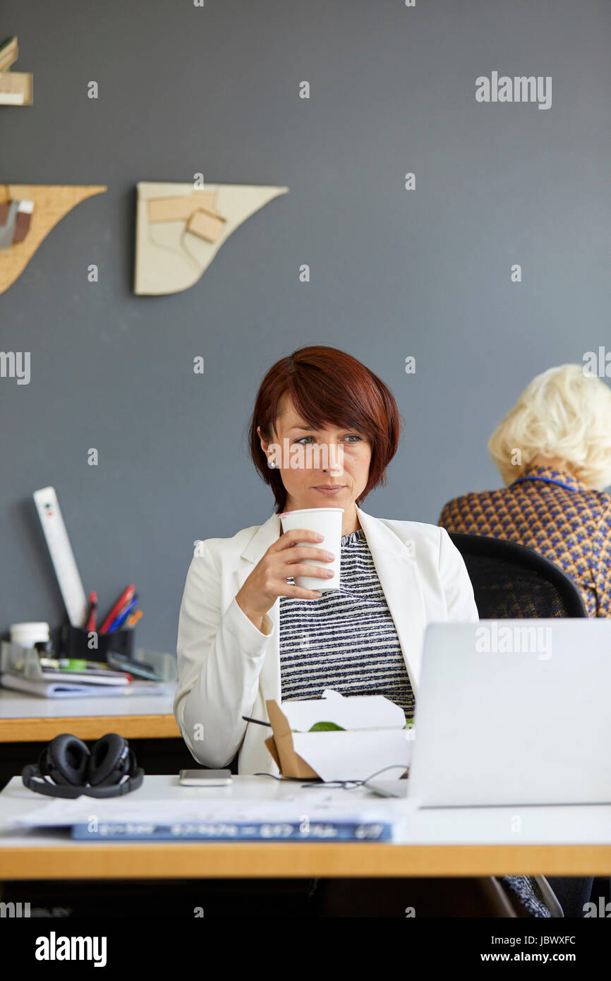 Diseñador femenina mirando portátil y beber café en la oficina Foto de stock