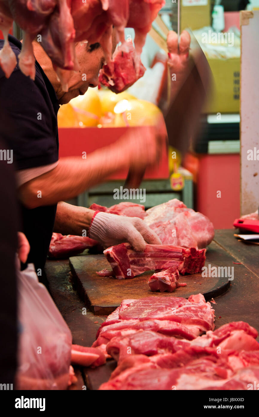 Retrato vertical de un carnicero que corta piezas de carne en un mercado húmedo en Hong Kong, China. Foto de stock