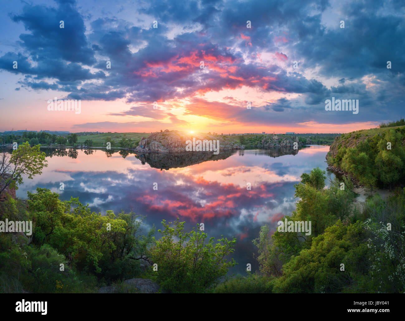 Hermosa escena con río, verdes árboles, rocas y el increíble cielo azul con nubes de colores reflejados en el agua al atardecer. Fantástico paisaje de verano con Foto de stock