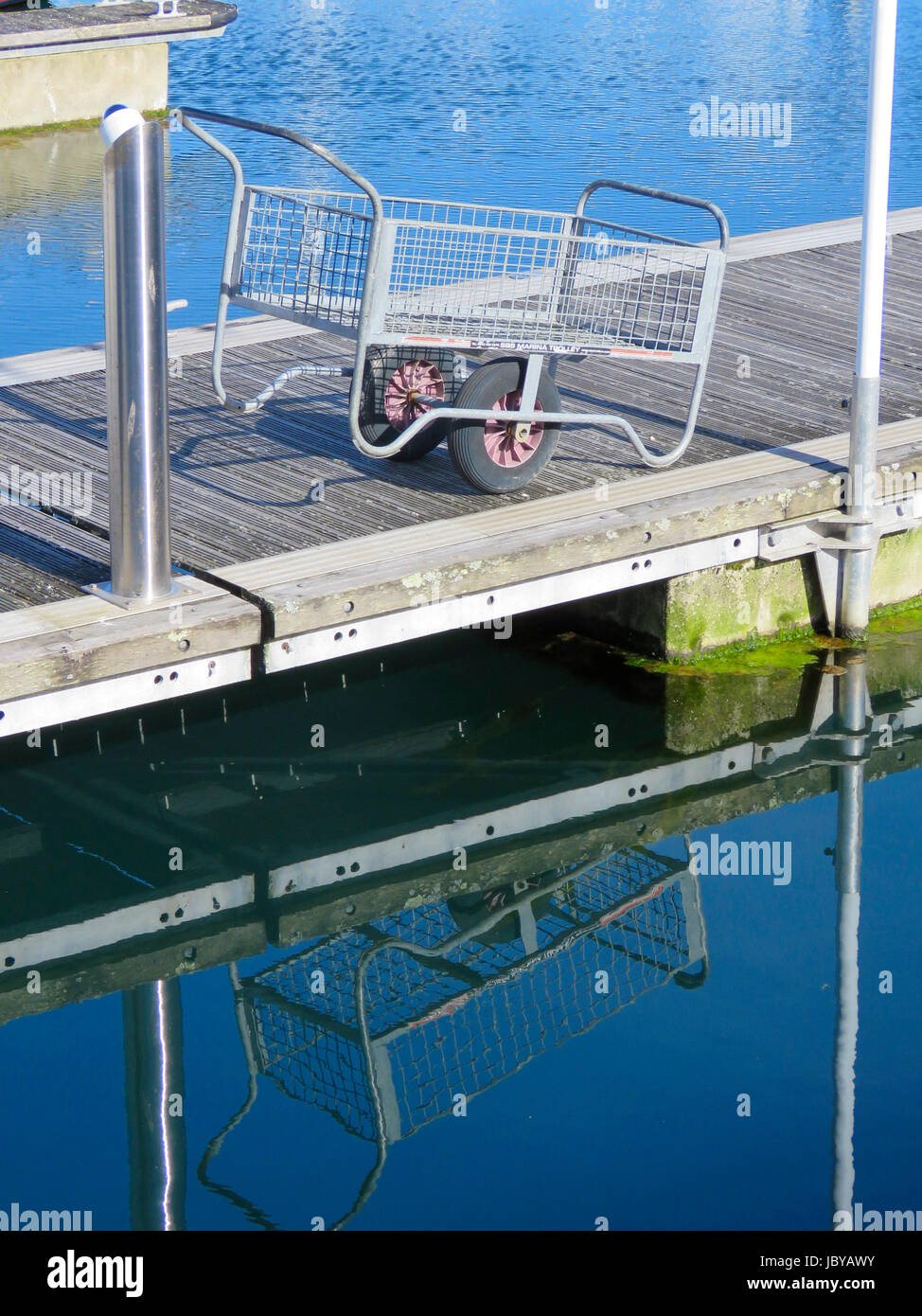 Carro de metal apoyado sobre pontón flotante en marina con reflejo en las aguas azules del mar, Sutton Harbour Marina, La Barbacana, Plymouth, Devon, Inglaterra. Foto de stock