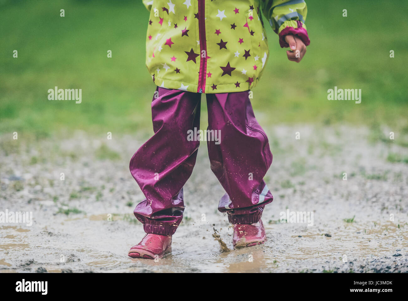 Los niños en botas de goma y ropa de lluvia saltando en charco. El agua  salpica los pies desde niñas como ella está saltando y jugando en la  lluvia. Protectores Fotografía de