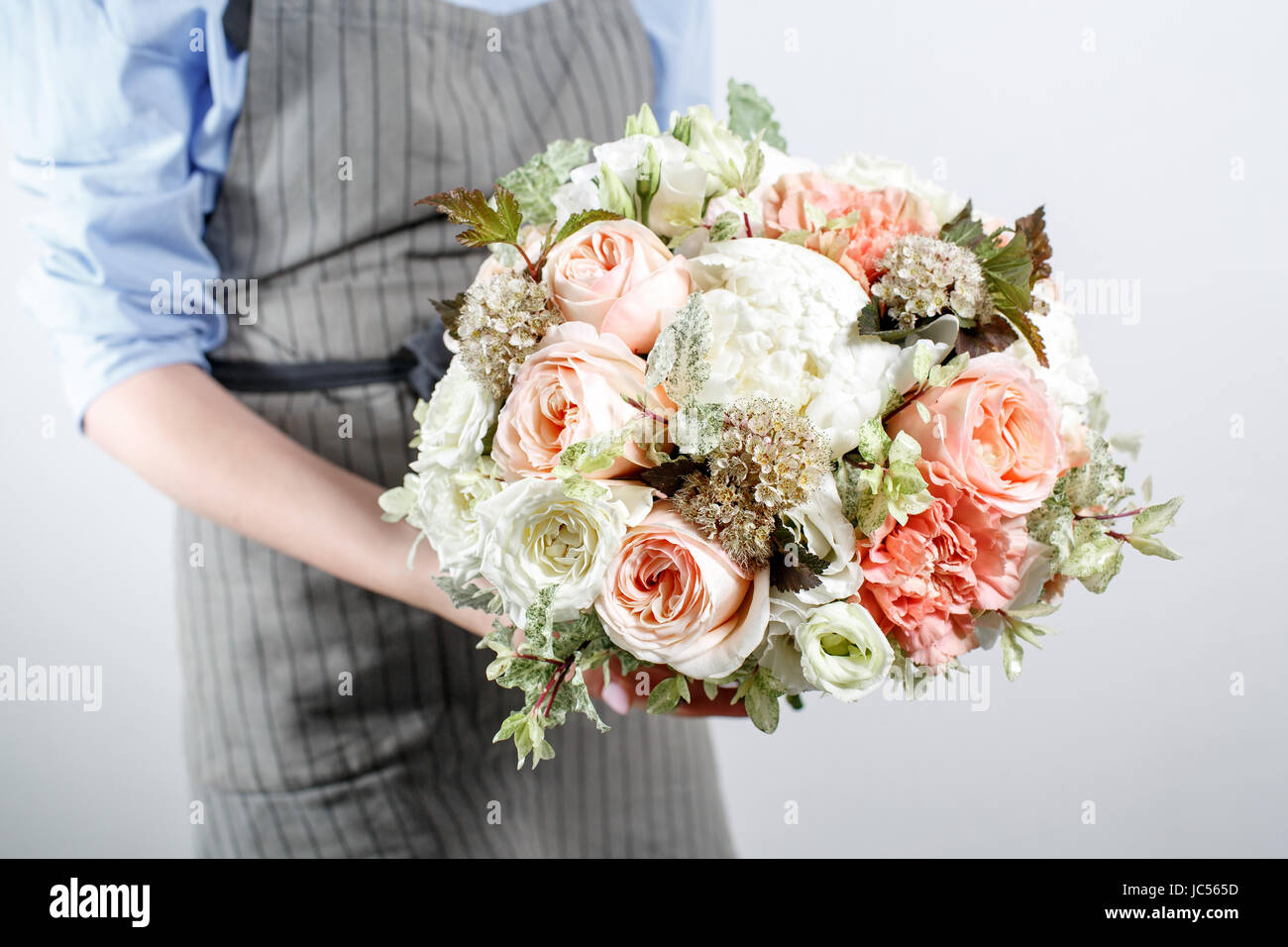 Precioso ramo de flores diferentes en el joven mano . colorida mezcla de  color de flor. Ropa de trabajo en una camisa azul y delantal gris  Fotografía de stock - Alamy
