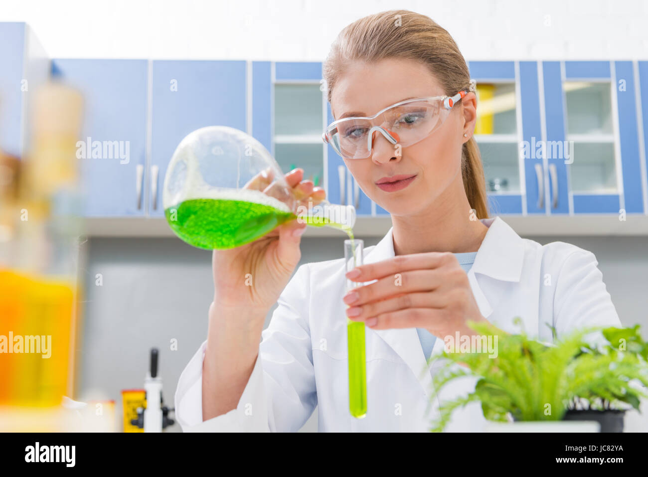 Young Scientist concentrada en gafas y bata blanca haciendo experimentos en el laboratorio Foto de stock