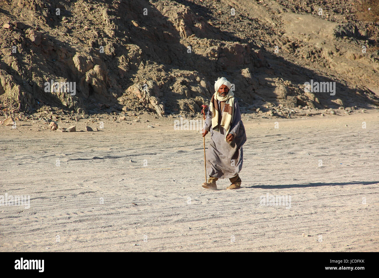 HURGHADA, EGIPTO - Abr 24 2015: el viejo Beduino con un palo, caminando por el desierto en el fondo de arena y montañas Foto de stock