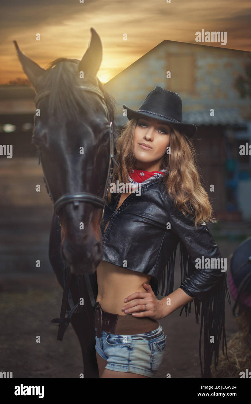 Chica cowboy en la black hat de pie cerca de caballo negro al atardecer  Fotografía de stock - Alamy
