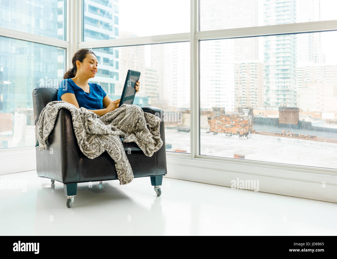 Mujer sentada en la silla por la ventana, día utilizando tablet digital. asiática, el pelo largo, adulto Foto de stock
