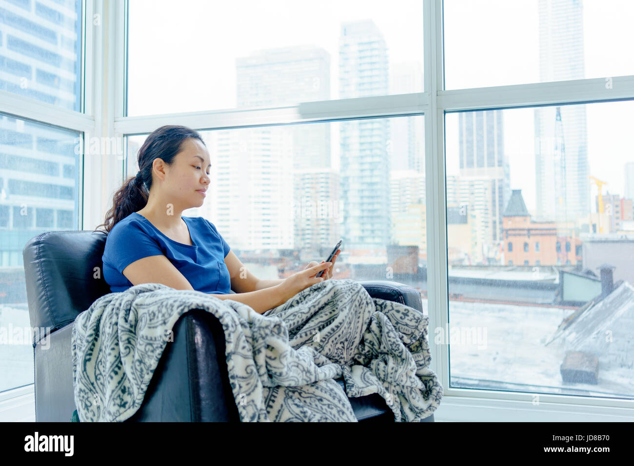 Mujer sentada en la silla por la ventana, día a través de teléfono móvil. asiática, el pelo largo, adulto Foto de stock