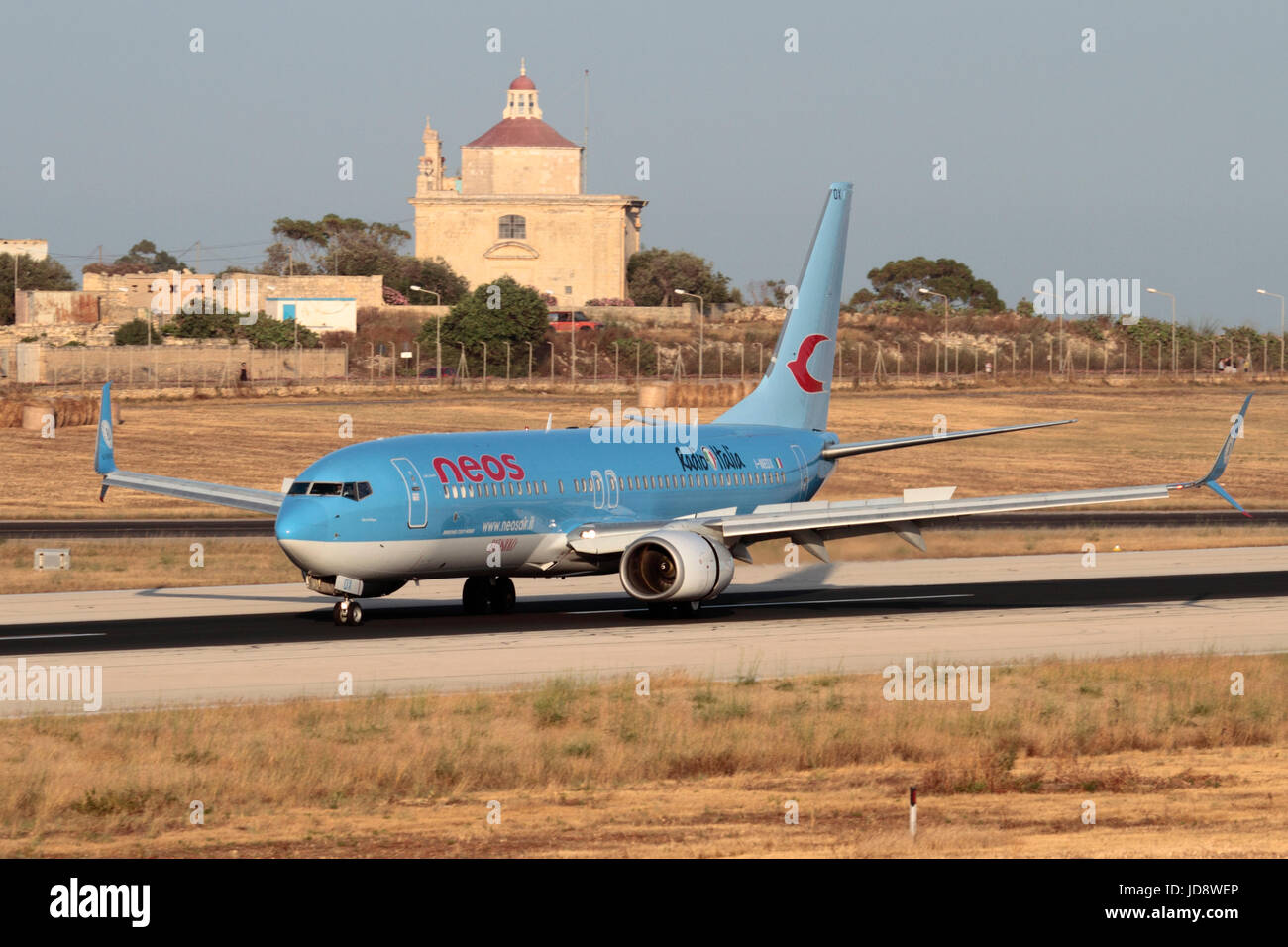 Los viajes aéreos en la UE. Neos vuelo Boeing 737-800 al aterrizar en la pista de aterrizaje en el aeropuerto de Malta, con Ta' Loretu capilla, Gudja, en el fondo Foto de stock