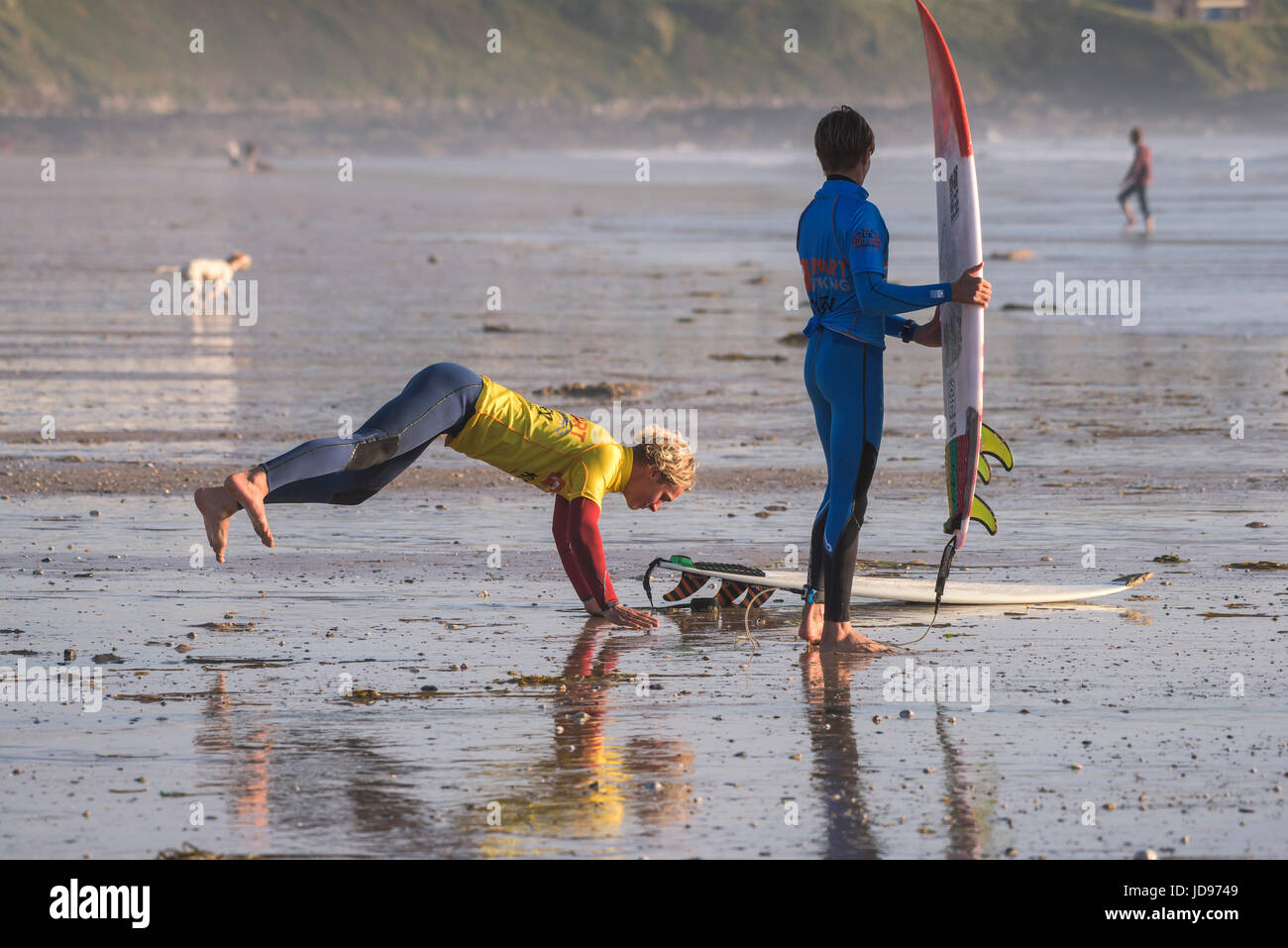 Dos surfistas que se estiran y hacen ejercicio antes de entrar en el mar. Playa Fistral, Newquay, Cornwall. Foto de stock