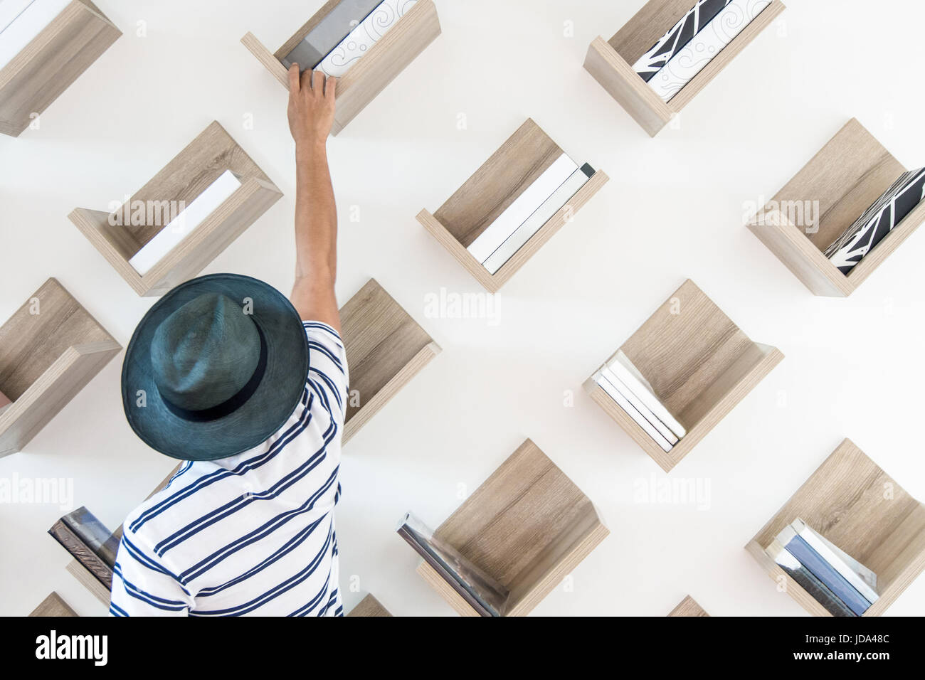 Un hombre está buscando el libro que quiere un bellamente decorado con una biblioteca de estantería y sillas de mimbre. Foto de stock