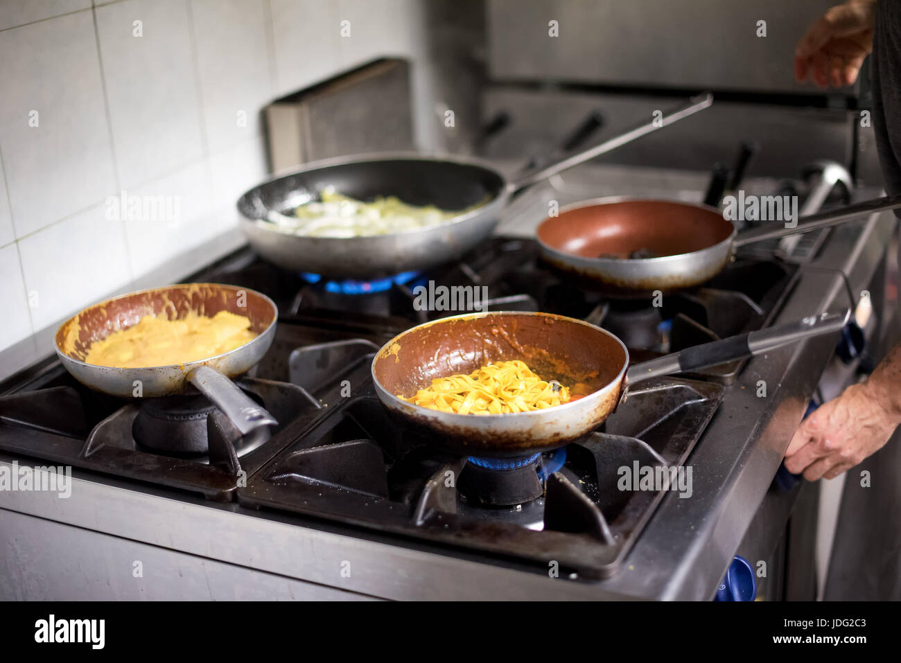 Cuatro sartenes con pasta italiana se cocinan sobre quemadores en el  restaurante y la cocina del chef manos ajustando la temperatura Fotografía  de stock - Alamy