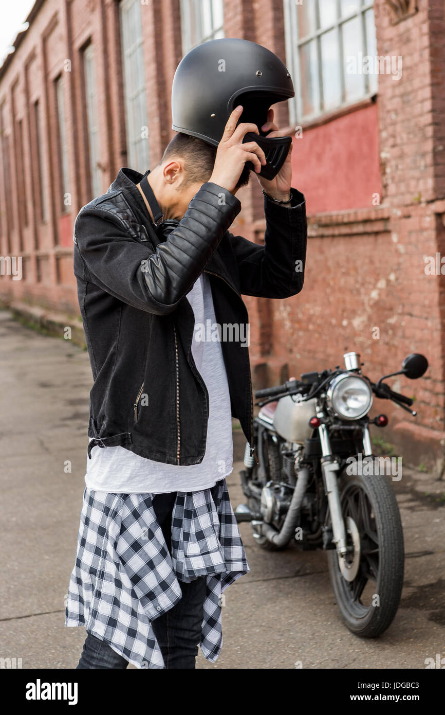 Guapo rider biker hombre en chaqueta de cuero negro y jeans ponerse el  casco cerca de estilo clásico cafe racer moto. Moto custom made en vintage  garaje Fotografía de stock - Alamy