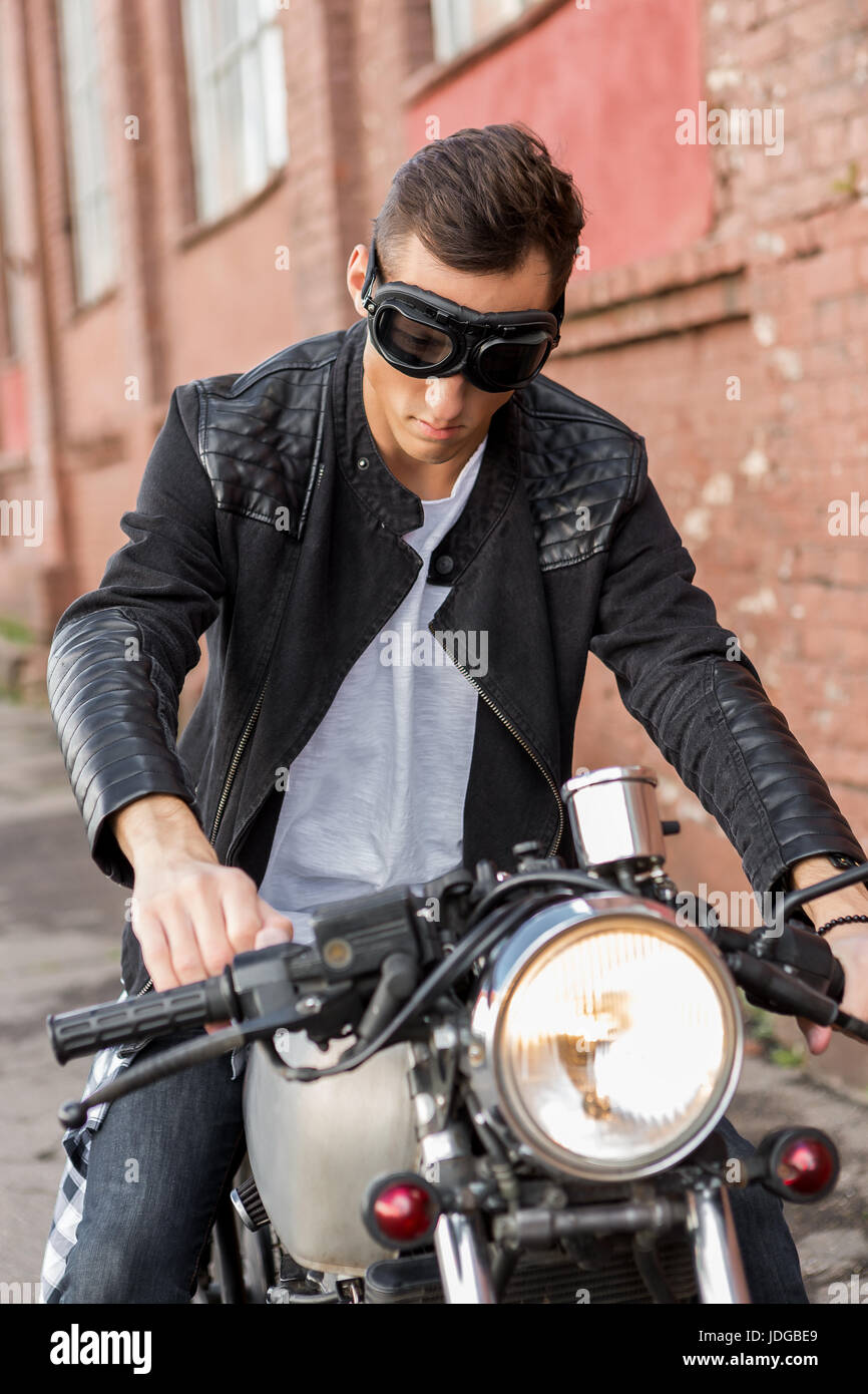 Guapo rider biker hombre en chaqueta de cuero negro y protección sentarse en estilo clásico racer moto. Moto custom made en vintage garaje Fotografía de stock - Alamy