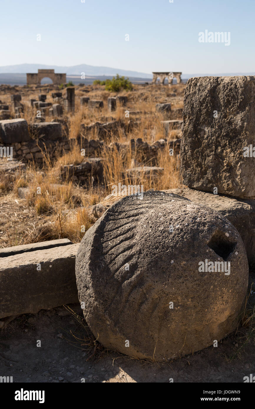 Una gran piedra tallada, posiblemente parte de un molino, mentiras contra un muro en las ruinas romanas de Volubilis rown en Marruecos Foto de stock
