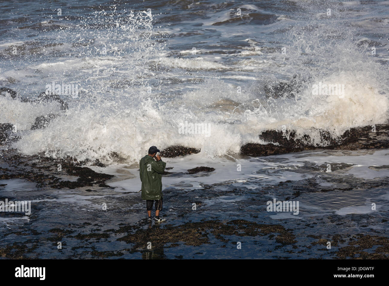 Un hombre espera una brecha entre el Atlántico grandes olas rompiendo en la orilla a marisquean Foto de stock
