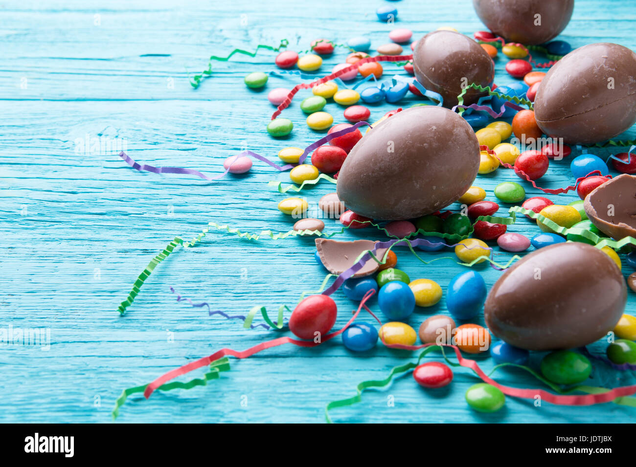 Huevos de chocolate, gominolas, cintas de colores sobre la mesa de madera azul Foto de stock