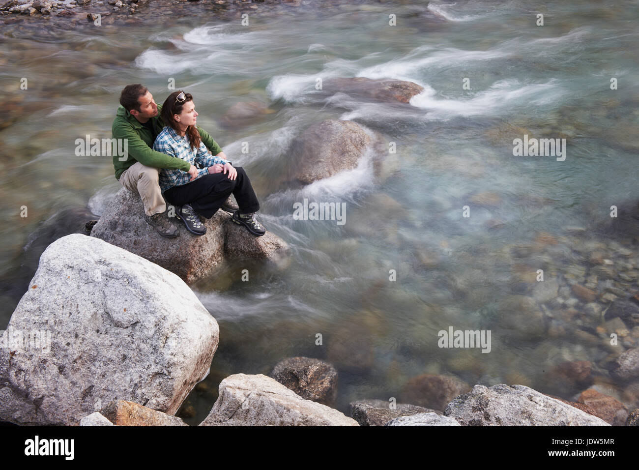 Adulto medio pareja sentada sobre las rocas en el río. Foto de stock