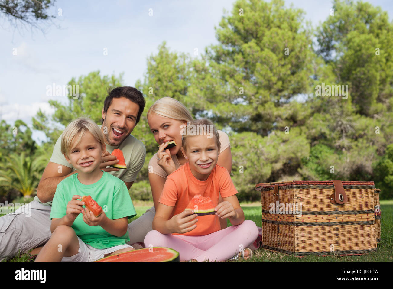 Familia feliz tener un picnic y comiendo sandía retrato en el parque en un día soleado Foto de stock
