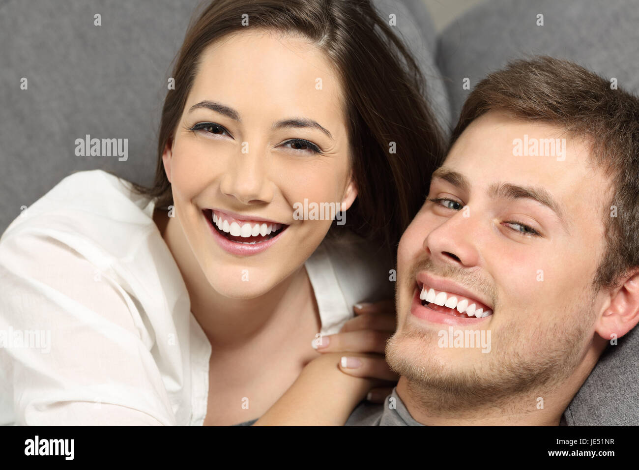Feliz pareja con dientes perfectos y sonrisa blanca, acostado en un sofá y mirando a usted Foto de stock