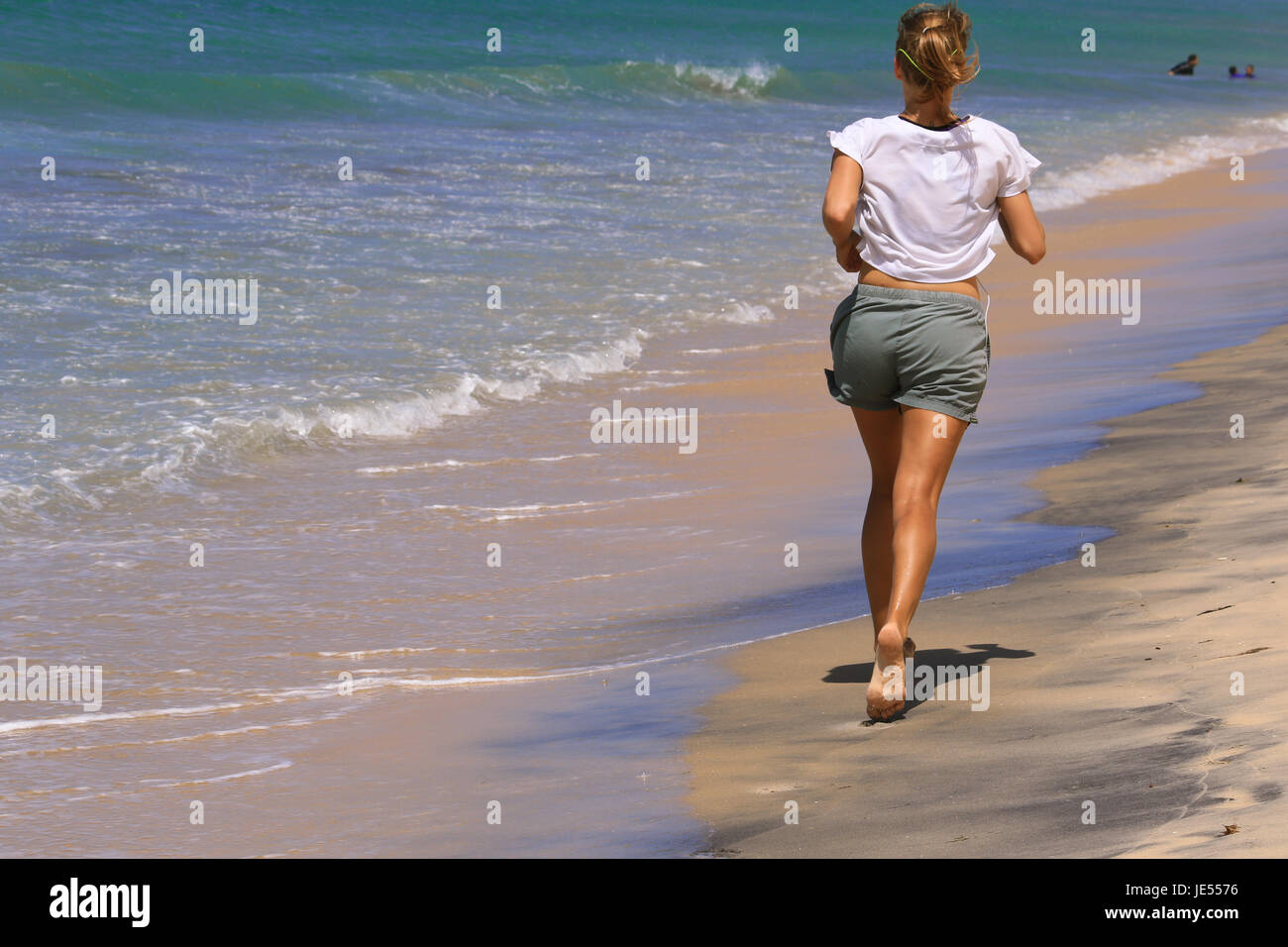 Chica deportiva está funcionando a lo largo de la playa del océano para mantener el cuerpo perfecto para Foto de stock
