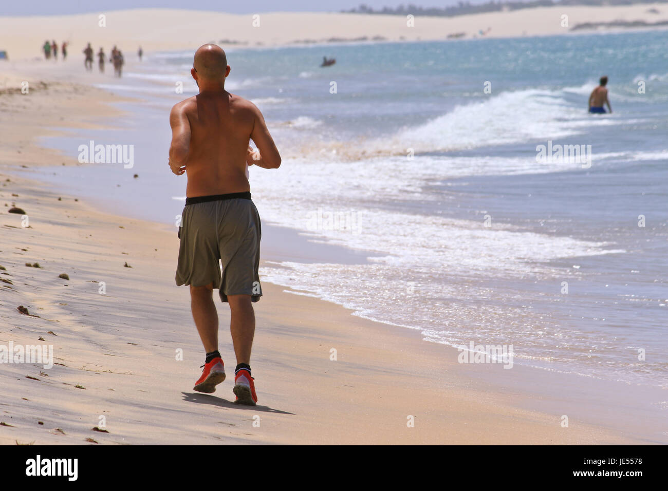 Hombre deportiva está funcionando a lo largo de la playa del océano para mantener el cuerpo perfecto para Foto de stock