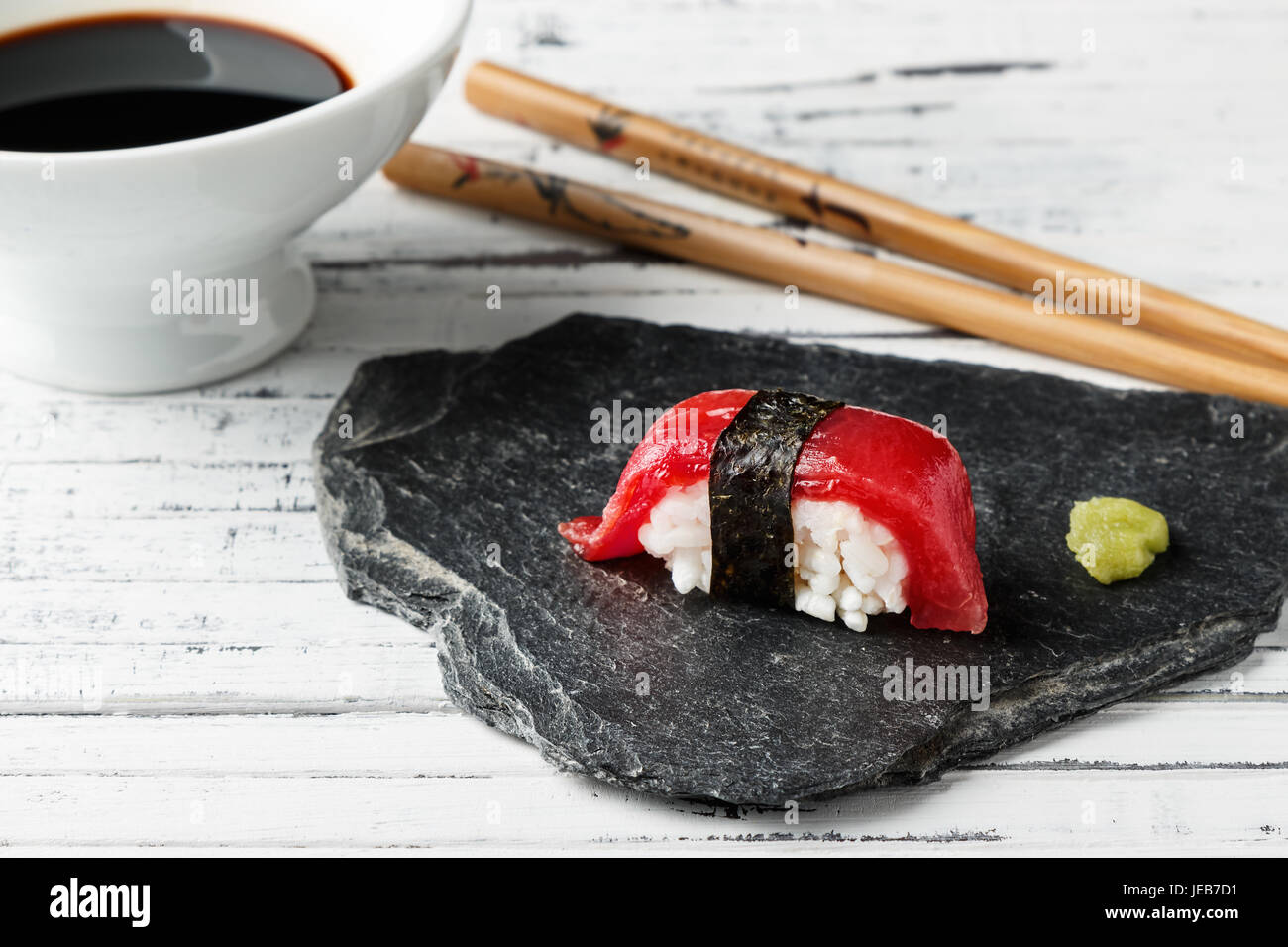 El nigiri de atún rojo con alga nori y wasabi pegar en piedra pizarra. Los  palillos y el tazón con la salsa de soja en el fondo de casco de madera  blanca.