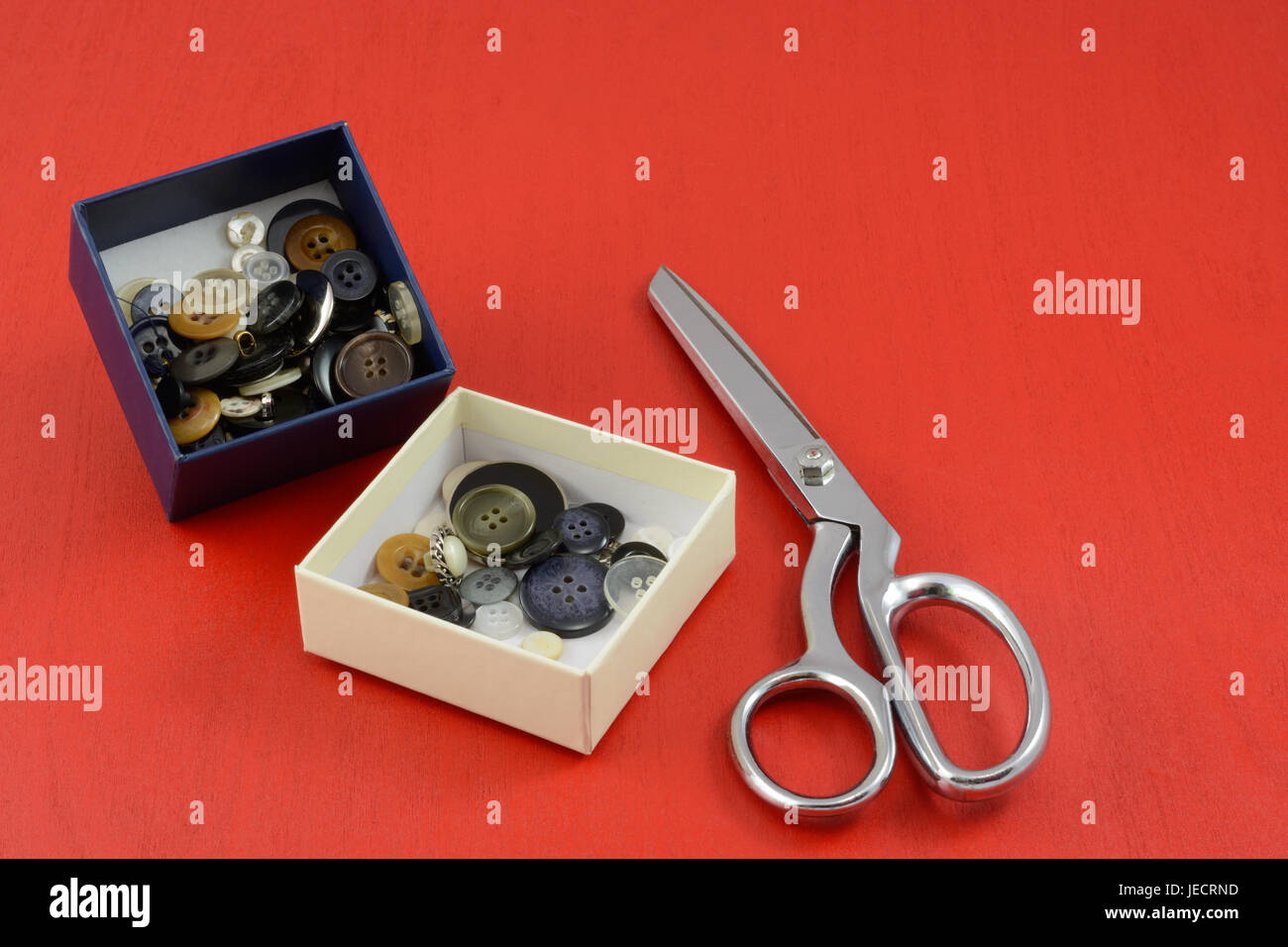 Colección de botones en cuadros blancos y azules y tijeras de metal sobre fondo de madera roja Foto de stock