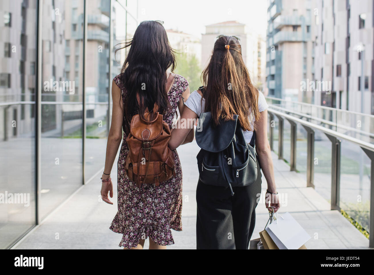 Dos mujeres jóvenes con mochilas y bolsas de compras caminando en la ciudad de stock - Alamy