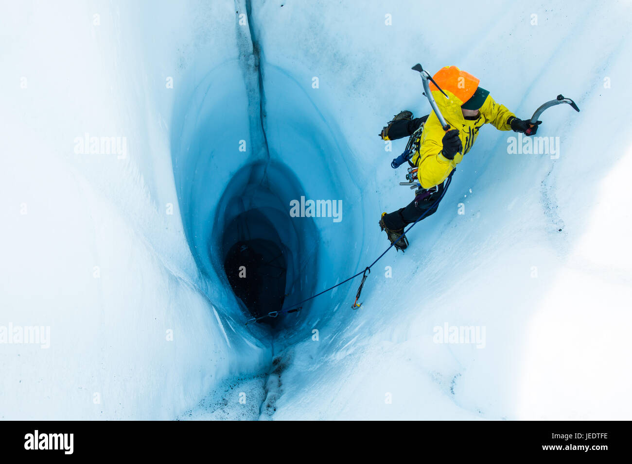 Un hombre llevando un ice climb fuera de una gran moulin o un agujero en el hielo del Glaciar Matanuska en Alaska. Para comenzar la ascensión, él y su belayer rappell Foto de stock