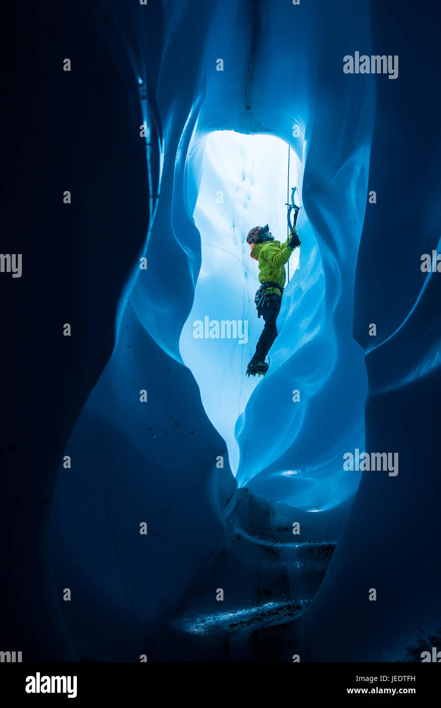Un escalador de hielo dentro de un gran túnel de hielo en la parte inferior de un molino. Él está subiendo hacia la parte superior del agujero de entrada Foto de stock