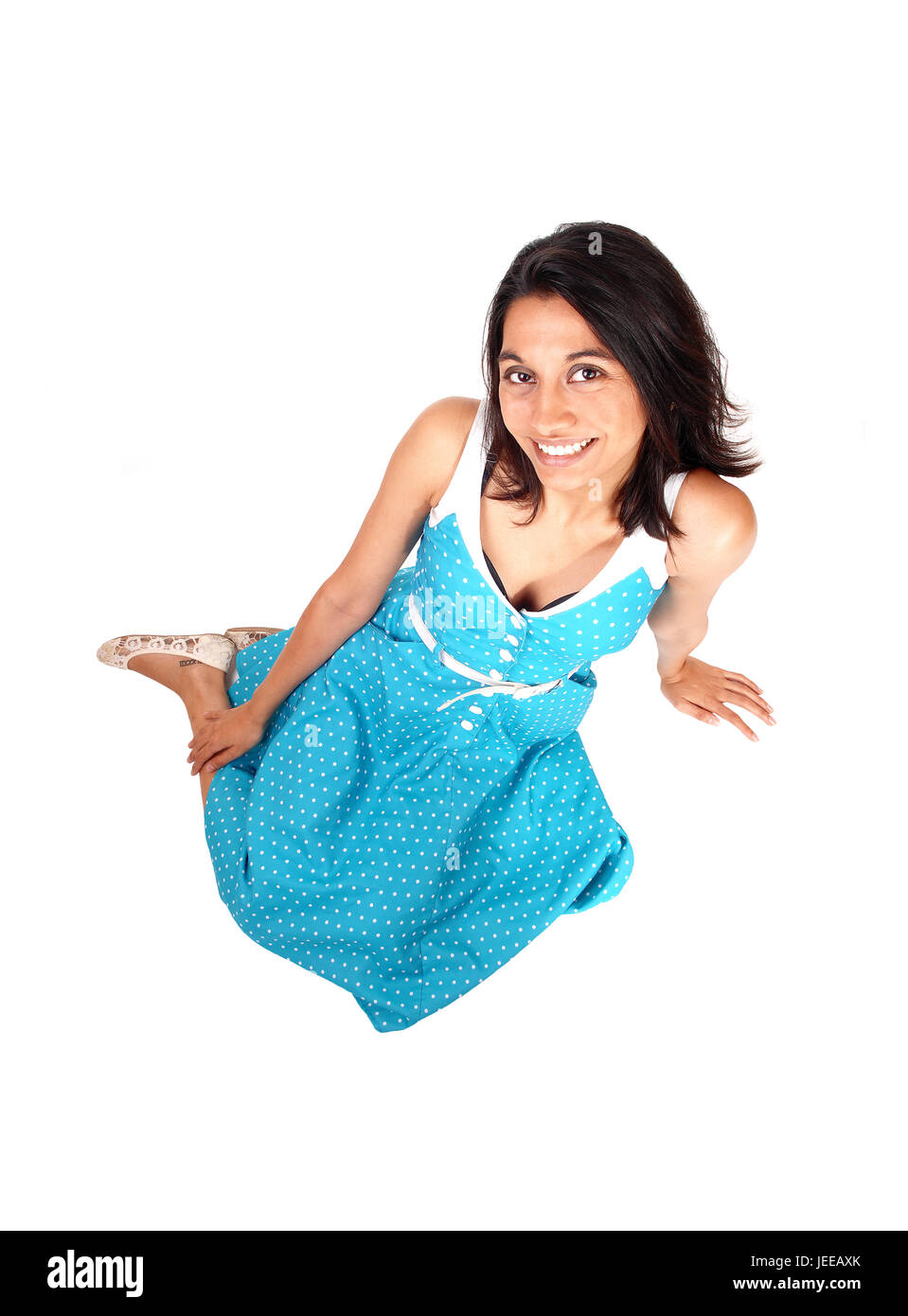 Una hermosa joven hispana sentado en un vestido azul en el suelo, sonriente, aislados en fondo blanco. Foto de stock