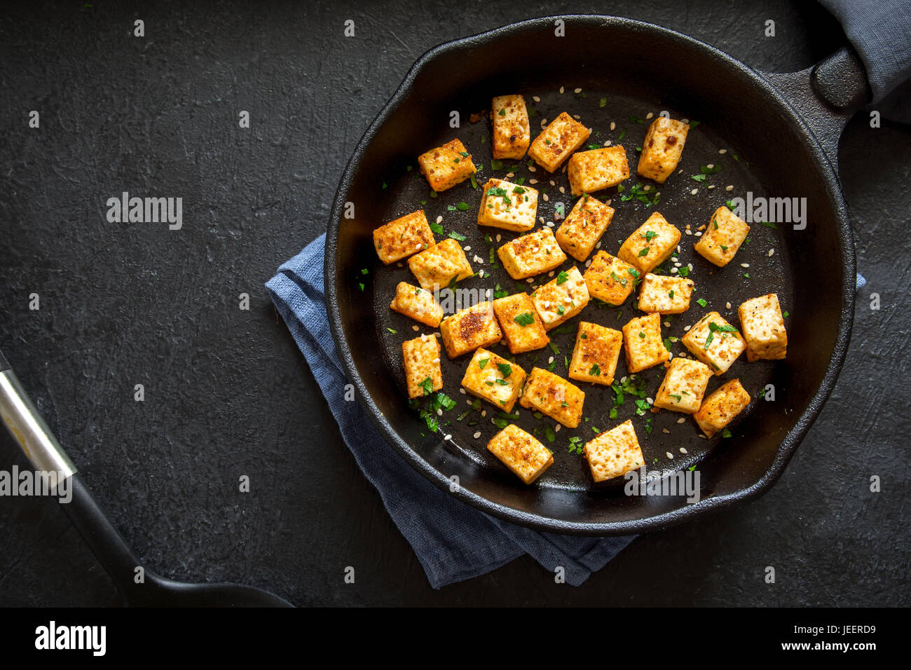 Tofu frito con semillas de sésamo y especias en sartén de hierro fundido,  copie el espacio. Ingrediente saludable dieta vegetariana vegana para  cocinar los alimentos. Tofu asado sobre bla Fotografía de stock -