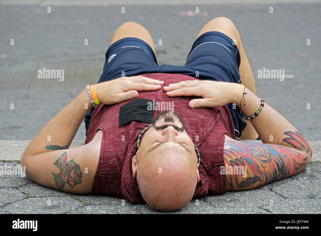 Foto de un hombre descansando con tatuajes, vistiendo un tank top fotografiado desde un ángulo inusual. Foto de stock