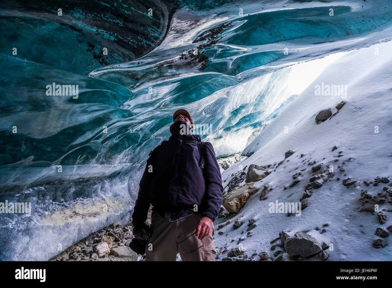 Un hombre busca en el hielo del glaciar Canwell mientras está de pie en la entrada a la cueva de hielo, Alaska, Estados Unidos de América Foto de stock