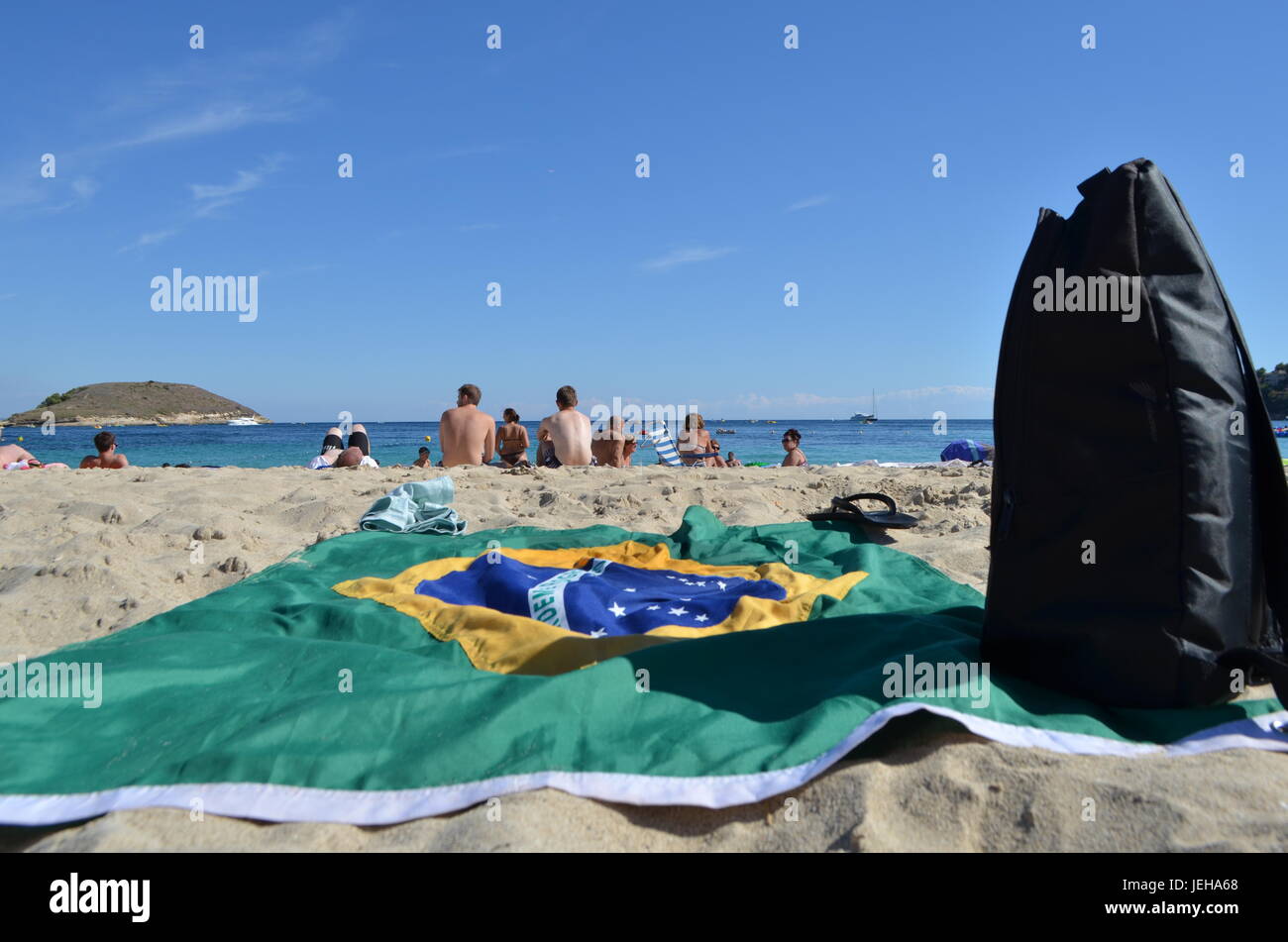 Estirado bandera de Brasil y una mochila negra sobre la arena de la playa de la Barceloneta en Barcelona, España Foto de stock