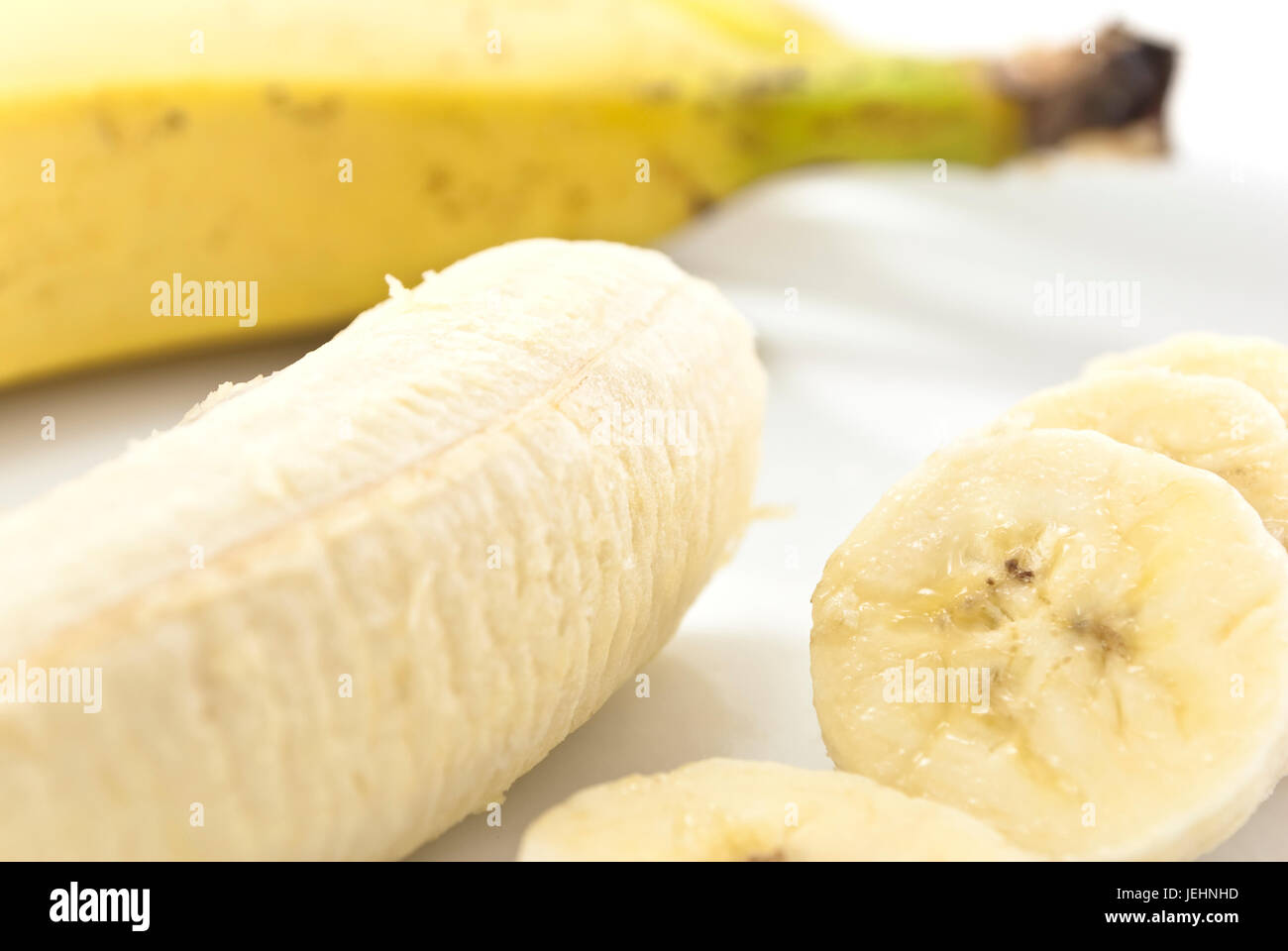 Primer plano de rodajas de plátano sobre una placa de china, junto con la porción restante de plátano pelado, con una cáscara de banana en foco suave en el fondo. Foto de stock