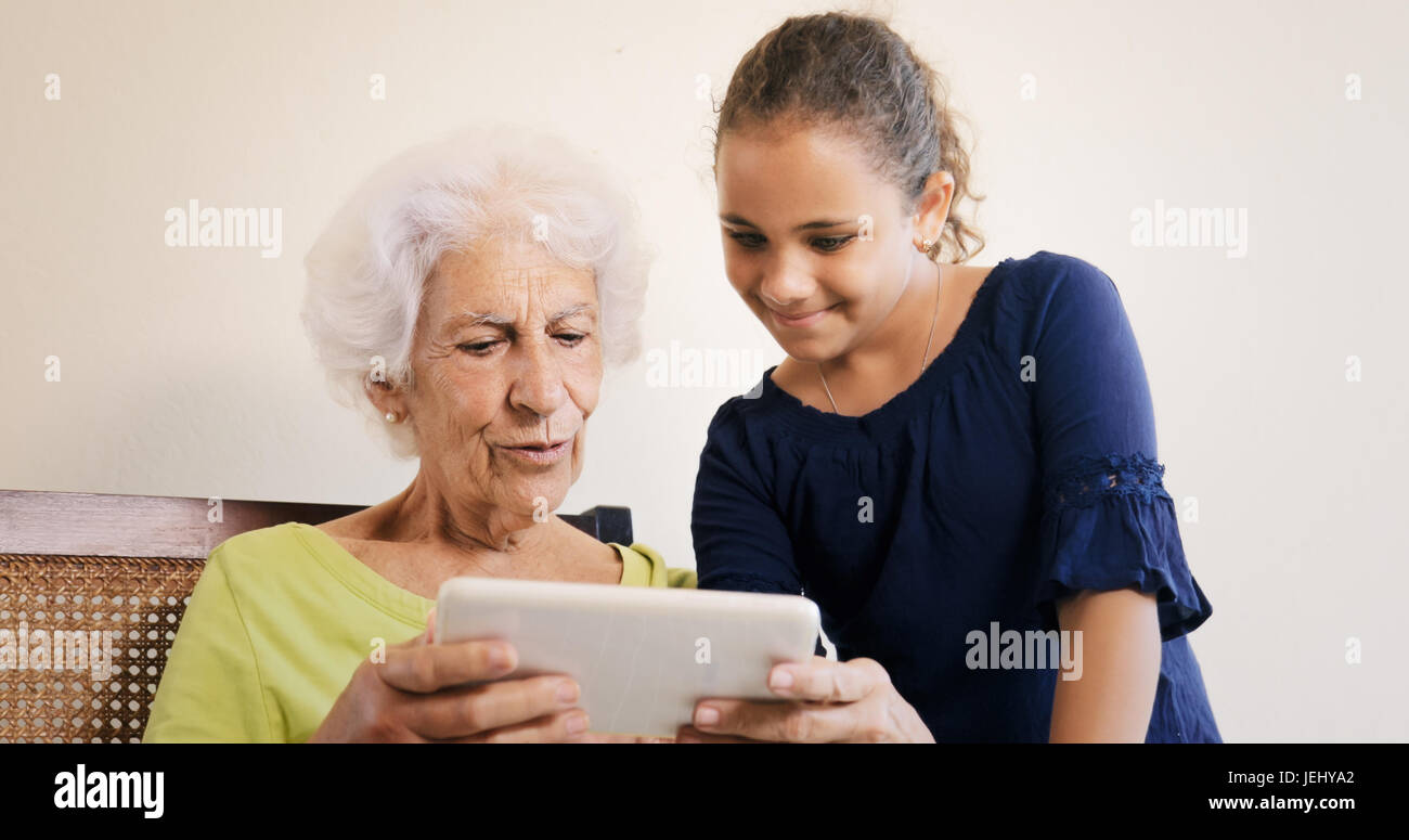 Relación Familiar entre abuela y nieta. Bond, afecto y amor, abuela y nieto hembra que navegan por la Web con tablet en casa Foto de stock