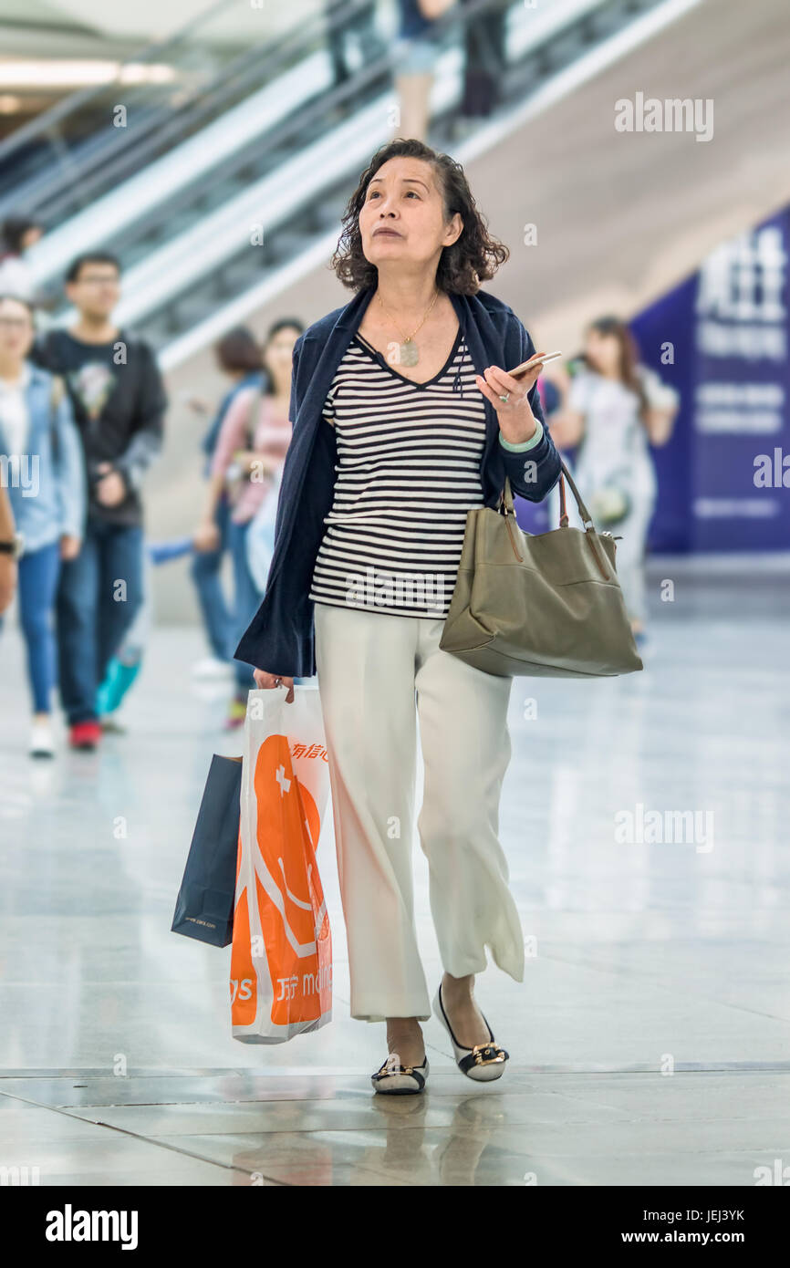 BEIJING-15 DE MAYO DE 2106. Mujer vieja con estilo y vestida con bolsas de compras caminando en el interior del lujoso centro comercial. Foto de stock