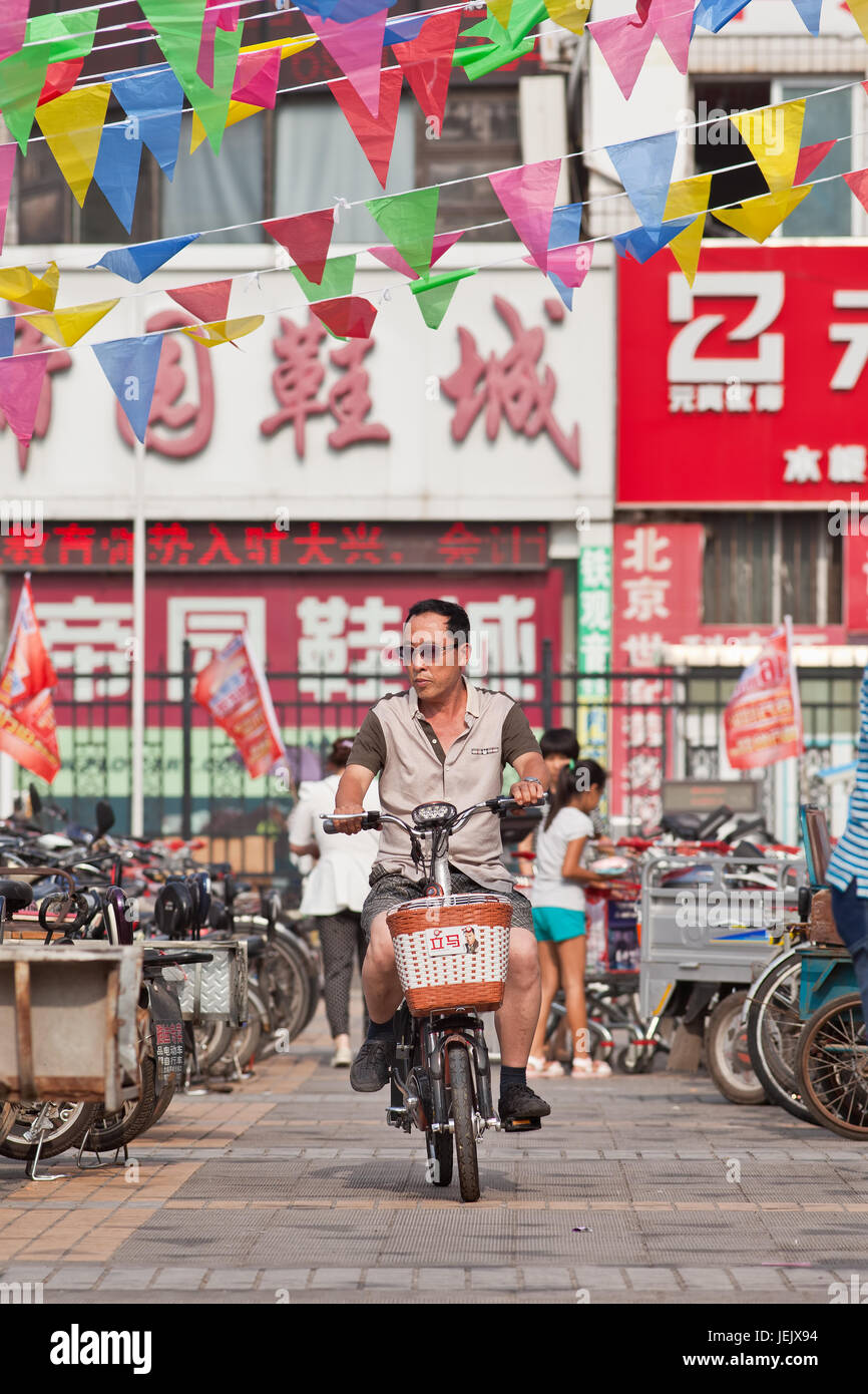 BEIJING-24 DE JULIO DE 2015. Hombre en e-bike en la zona comercial. En una década, las bicicletas electrónicas en China subieron de casi cero a 150 millones (2015). Foto de stock