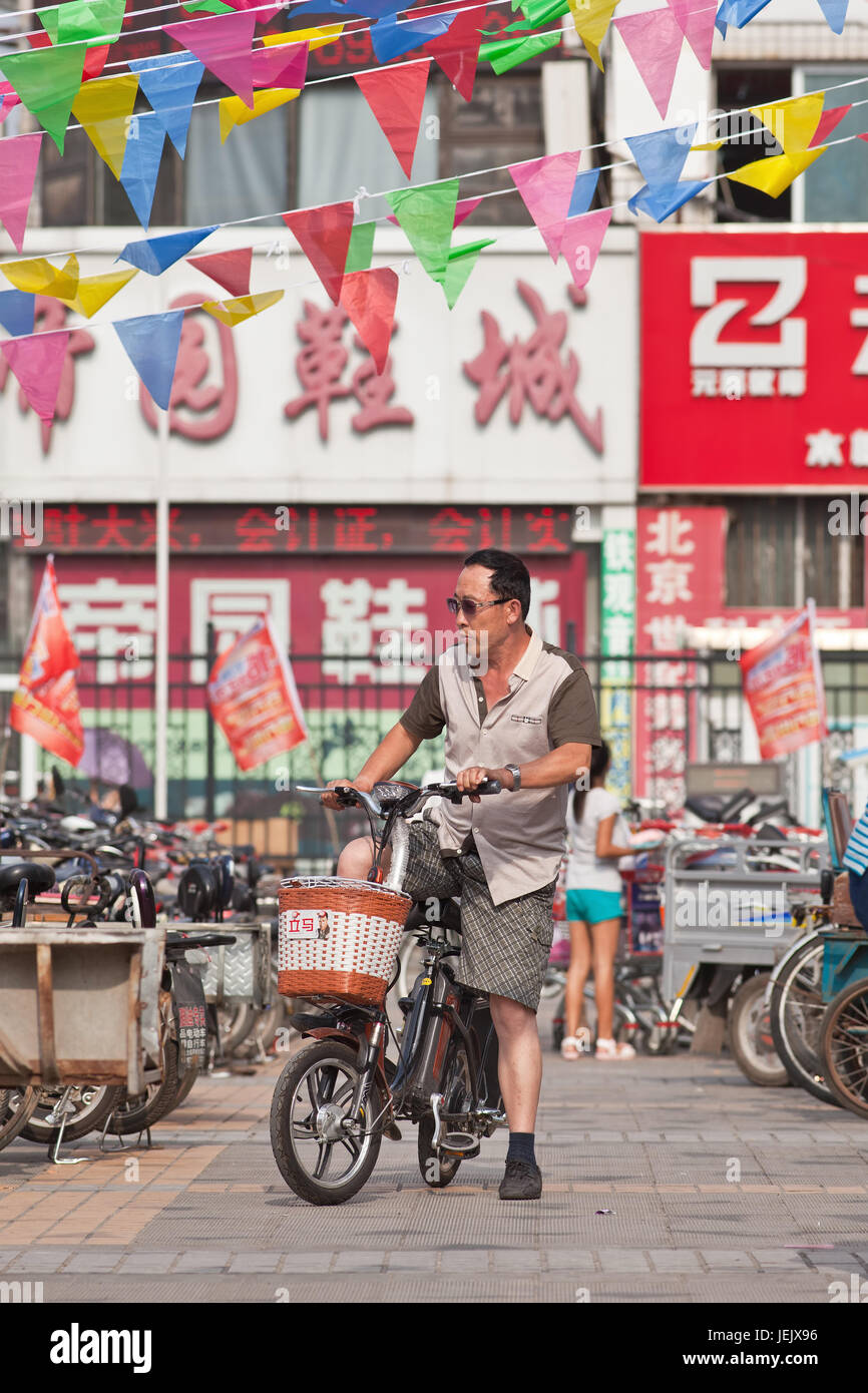 BEIJING-24 DE JULIO DE 2015. Hombre en e-bike en la zona comercial. En una década, las bicicletas electrónicas en China subieron de casi cero a 150 millones (2015). Foto de stock